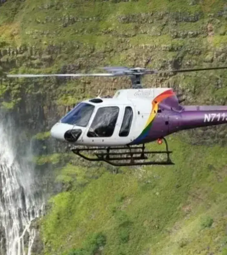 Helicopter flying near waterfall and green cliffs in Hawaii