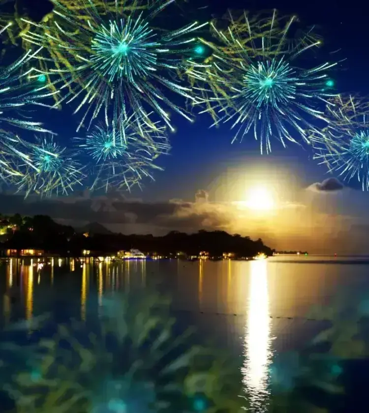 Colorful blue fireworks over a Hawaiian coastal resort at night with moonlight reflecting on calm water