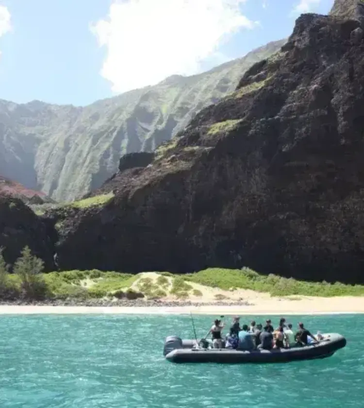 Boat with tourists floating on turquoise water near rocky beach and tall cliffs