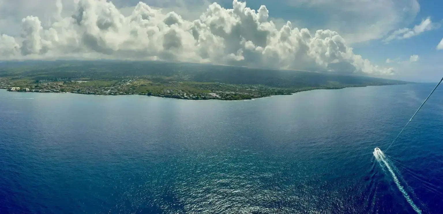 Aerial view of coastline under cloudy sky with a small boat on blue ocean