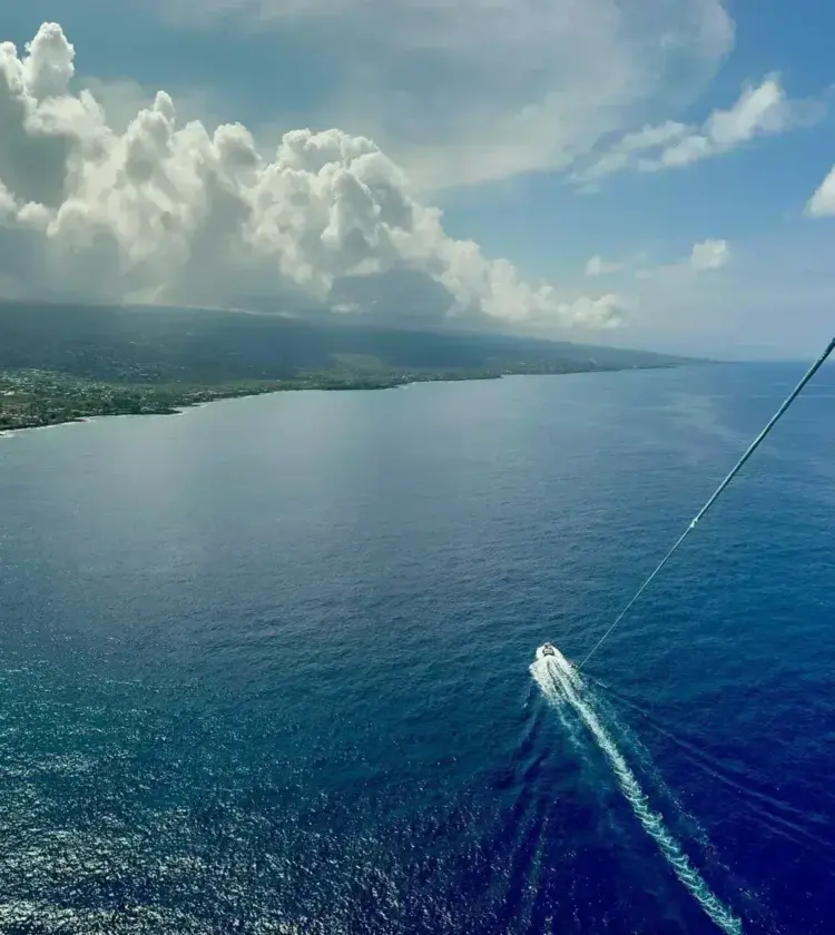 Aerial view of coastline under cloudy sky with a small boat on blue ocean