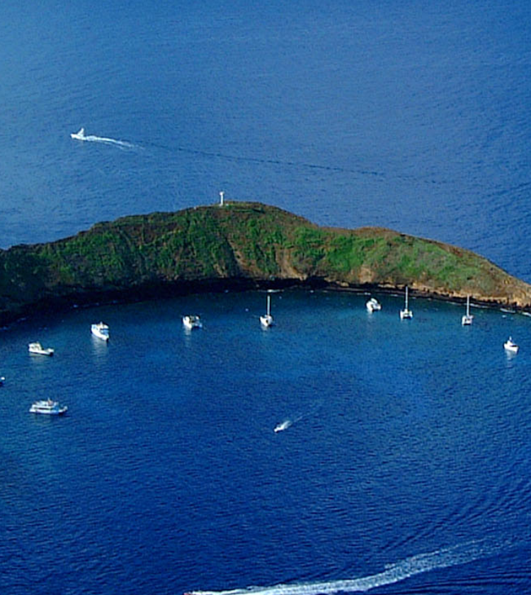 volcanic island surrounded by deep blue ocean with boats anchored inside curved bay