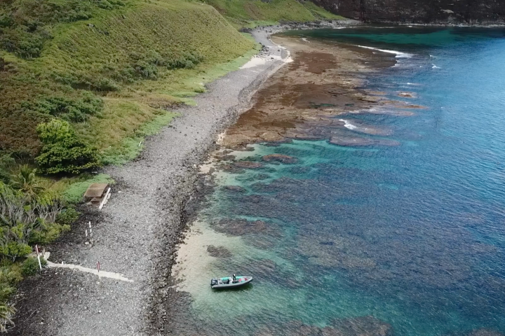 Boat anchored near rocky coastline with clear turquoise water and coral reef