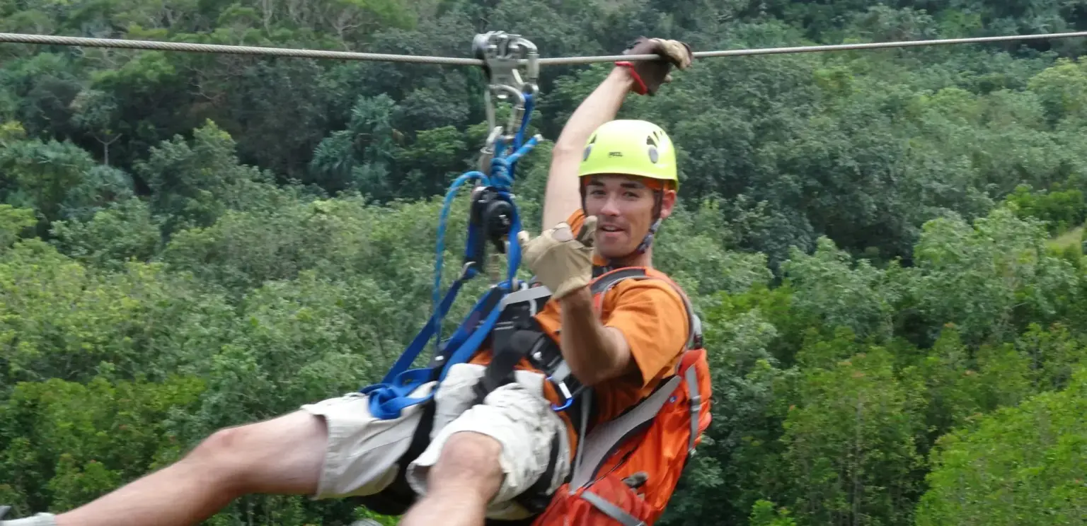 man ziplining in forest wearing yellow helmet orange backpack