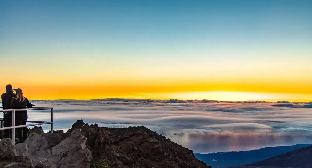 Couple observing sunset over clouds from volcanic summit ridge
