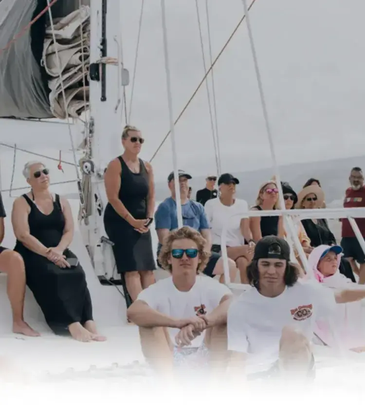 diverse group of people sitting and standing on a sailboat under cloudy sky